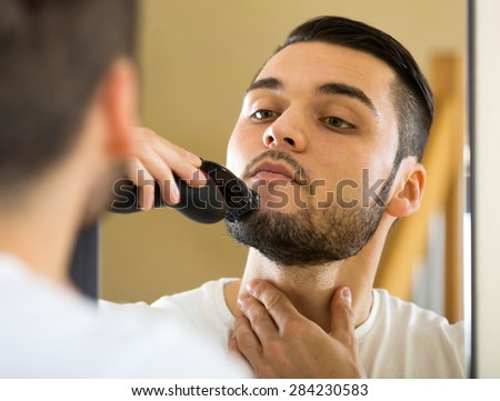 Young guy shaving by electric shaver at home