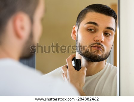 Young handsome guy using perfume in front of mirror