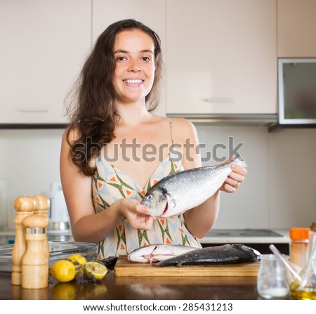 Happy young girl holding raw fish at kitchen
