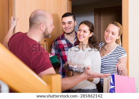 Cheerful smiling guests with cake and presents standing in doorway