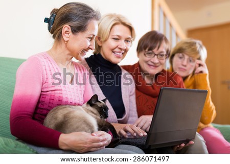 Cheerful smiling aged women working with notebook using wifi on sofa