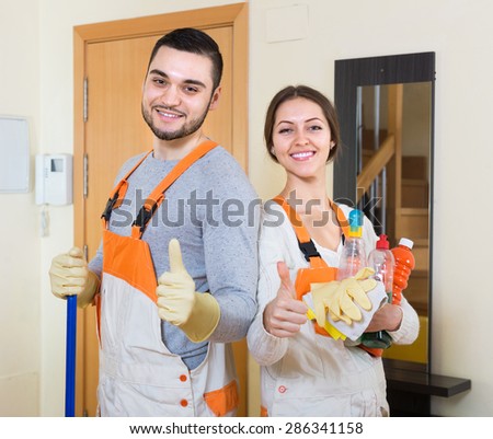 Portrait of smiling professional cleaners with equipment at door of client house