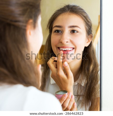Portrait smiling girl looks in the mirror and uses lip balm