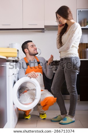 Young woman showing broken washing machine to smiling repairman