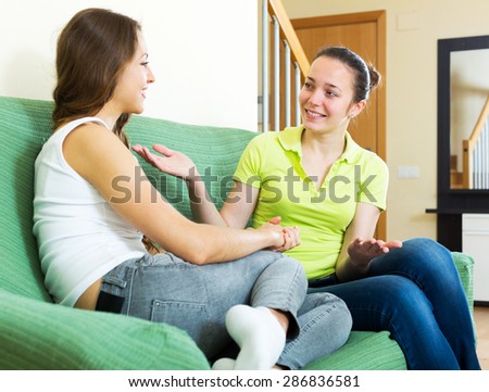 two cheerful woman talking on sofa in home interior. Focus on the right woman