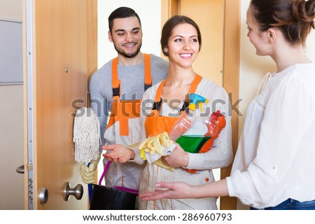 Happy housewife meeting cleaning crew at apartment doorway. Focus on woman