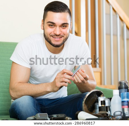 Young smiling handsome brunet doing manicure at home