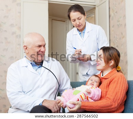 Elderly doctor examining little child in the arms of mother. Nurse writes symptoms