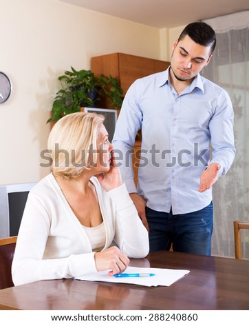 Upset senior woman and young boyfriend with invoices for payment. Focus on the woman