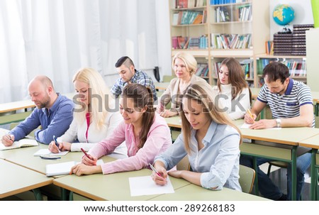 Attentive adult students industriously writing down the summary in classroom