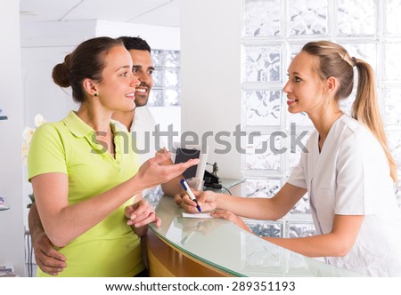 Young couple talking with secretary at reception in the clinic