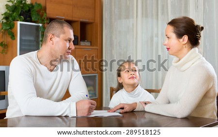 Sad family with little daughter reading financial documents at the table at home