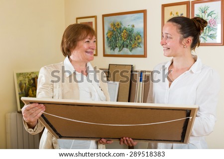 Two smiling women standing, looking at painting displayed in the hall