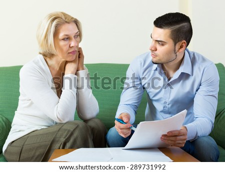 Sad senior woman questioning young man about letters from bank at home