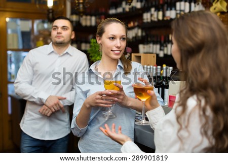 Two positive girls with man chatting at bar of restaurant