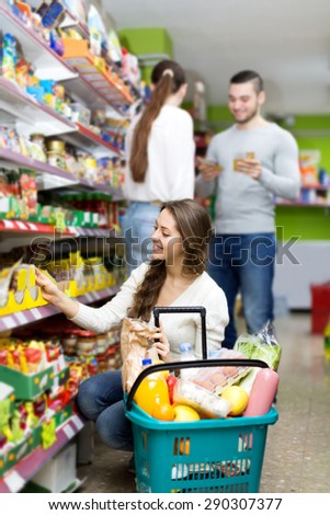 Smiling woman standing near shelves with canned goods at shop