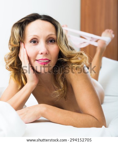 Smiling middle-aged blonde woman takes off underwear on bed