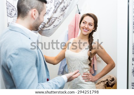 Cheerful smiling young couple with new apparel at fitting-room in clothing store