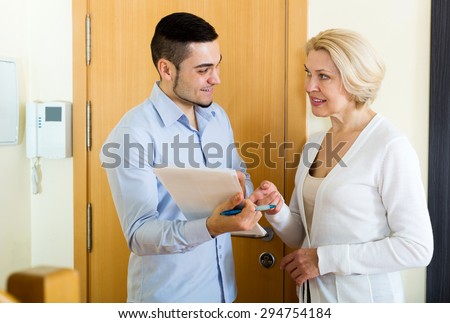 Cheerful mature woman answers the questions of adult employee  in door at home