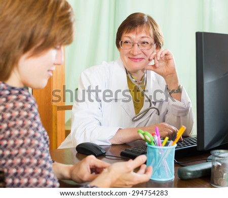 Ederly woman doctor  sitting at PC looking at patient friendly