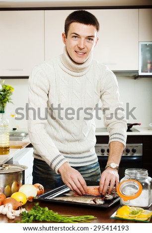Happy man cooking freshwater fish in sheet pan at kitchen table