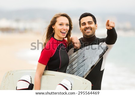 Happy adult couple running on the beach with surf boards. Focus on the woman