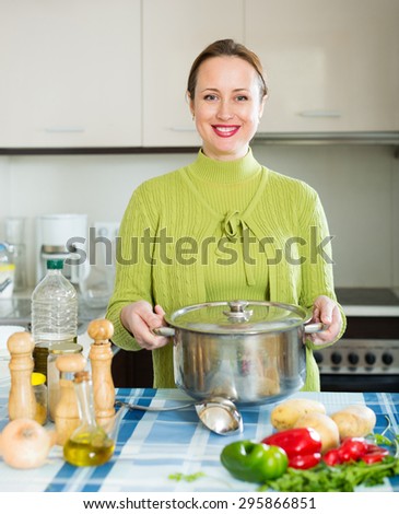 smiling girl with ladle cooking soup in domestic kitchen