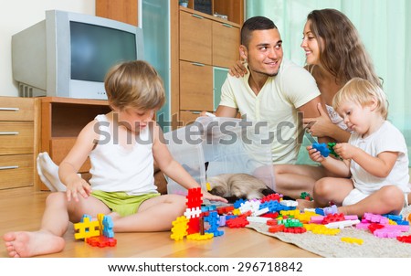 Happy smiling young parents and two daughters relaxing with toys in home