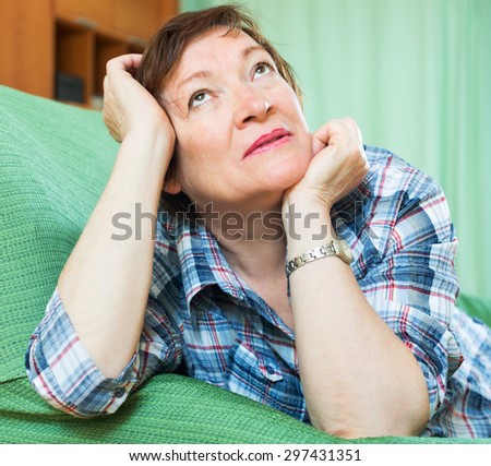 Stressed elderly woman laying on her elbows and thinking  on couch