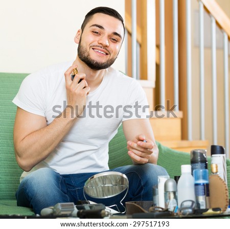 Young smiling handsome guy using perfume at home  for dating