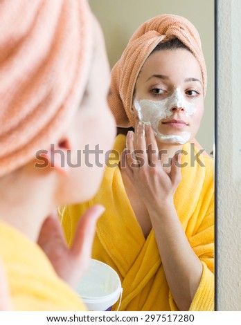 Young woman applying face pack in front of the mirror indoors