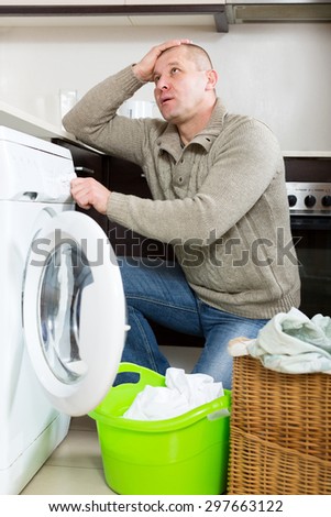 Home laundry. Sad guy using washing machine at home