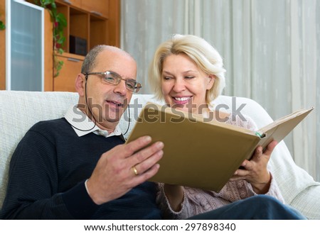 Portrait of loving senior spouses smiling with picture album at home. Focus on woman