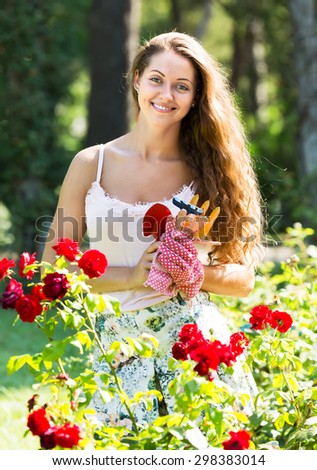 Smiling girl florist working in roses plants at summer garden