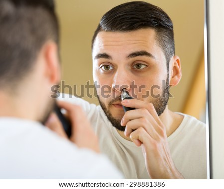 portrait handsome young man trims nose and ears hair at home