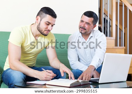 Smiling mature father helping son to do homework. Focus on the left man