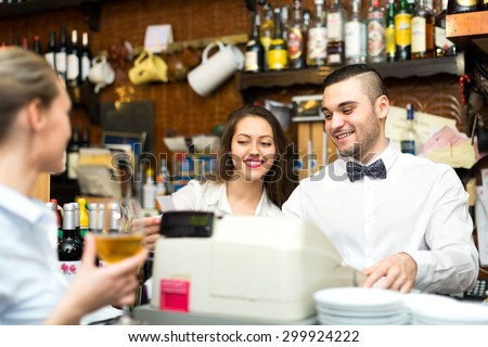 Friendly personnel working in a bar. A beautiful young waitress with a glass of wine, a bartender at a counter and administrator with a check