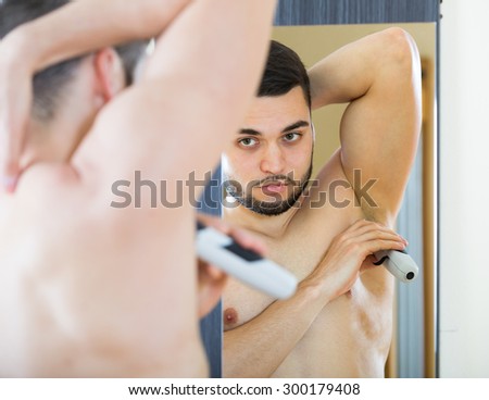 Man looking at mirror and shaving armpit with trimmer