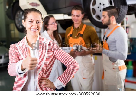 Portrait of a happy client at a car dealership with a beautiful smile and thumbs up sign with dealership crew on the background