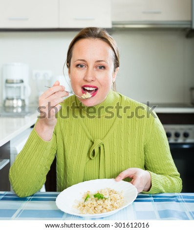 Smiling attractive healthy woman eating rice in the kitchen at home