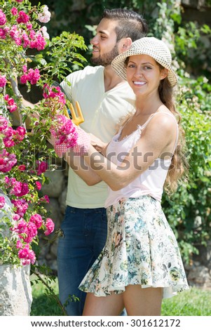 Young couple in flowers garden with horticultural sundry at summer day