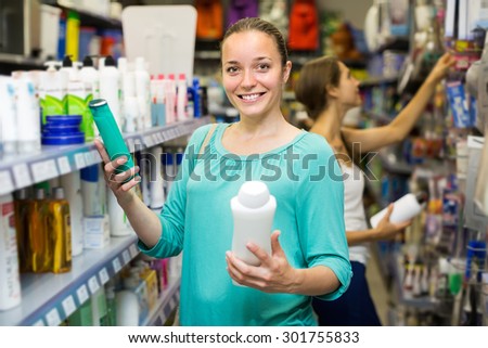 Cheerful smiling adult girl choosing shampoo at supermarket