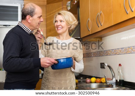 Elderly husband helping smiling wife to cook indoors