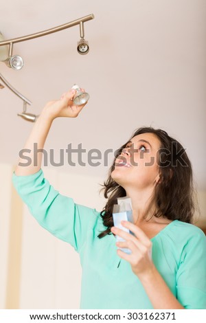 Happy smiling woman changing light bulb at her home