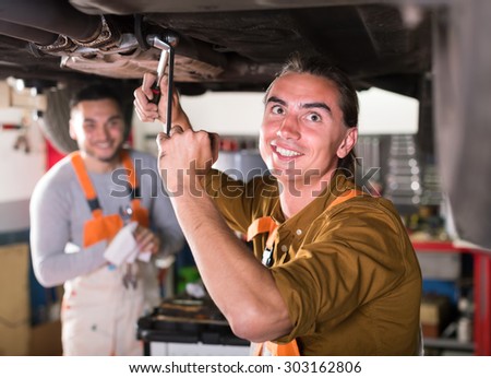 Serviceman at a dealership repairing exhaust system on a lifted up car