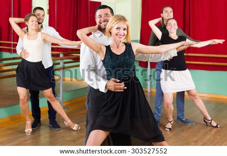 Group of happy young adults having tango class at dance studio. Selective focus