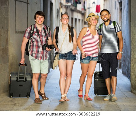 Company of happy travelers with travel bags walking the city
