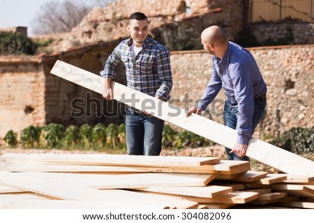 Two adult positive male builders carrying over plane boards at site