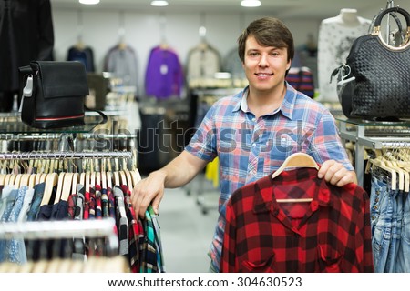 Young smiling guy choosing shirt at the clothing store