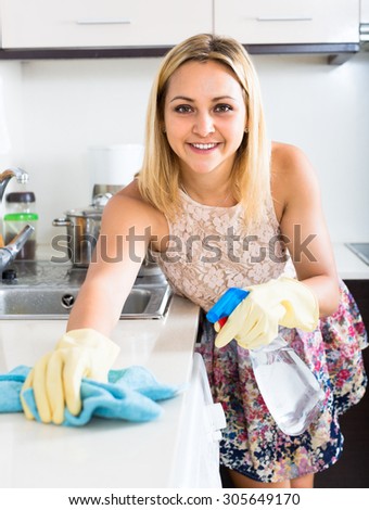 Happy young smiling housewife cleaning kitchen interior indoors